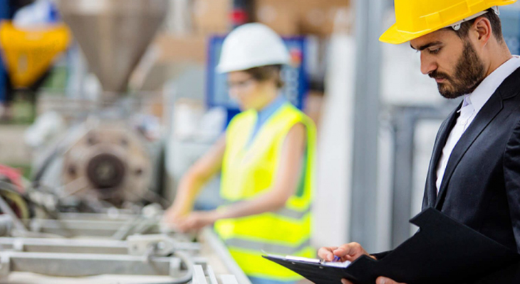 um homem analisando um equipamento industrial e uma mulher ao fundo